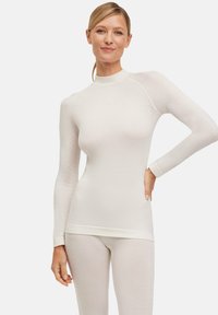 Maglietta termica a maniche lunghe in crema chiaro, con colletto alto, design aderente, texture senza cuciture e un delicato motivo sulle maniche.