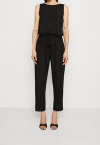 Mono negro sin mangas con escote redondo, cintura ceñida y pantalones de pierna ancha. Hecho de una tela suave y fluida.