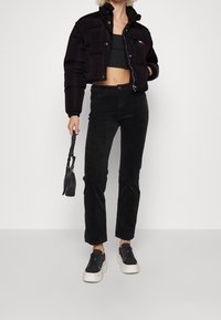 Sort polstret cropped jakke med høj krave, kombineret med sorte bukser i kordfløjl og chunky sorte sneakers. Lille sort håndtaske holdt i hånden.