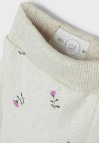 Tessuto di cotone chiaro con un colletto beige a coste, decorato con piccole ricami di fiori viola e un motivo testurizzato.
