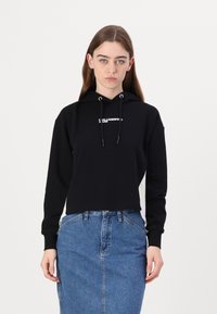 Hanorac negru scurt cu logo alb, glugă cu șnur și manșete ribbate, asortat cu o fustă din denim cu talie înaltă și detalii de cusătură.