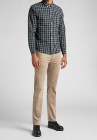 Camicetta a maniche lunghe a quadri blu e grigia, con colletto abbottonato. Abbinata a pantaloni in velluto a coste beige e stivali neri, presenta un design semplice.