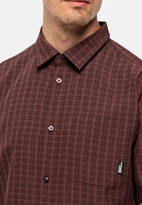 Bruin geruit shirt van stof met een zachte textuur. Bevat een button-down kraag, een borstzak en ronde plastic knopen.