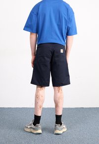 Blue cotton t-shirt, navy shorts with two back pockets and a small logo label. Gray sneakers with black socks. Light brown leg markings.