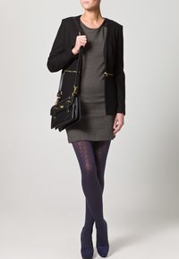 Černé na míru šité sako přes šedé šaty, doplněné námořnickými vzorovanými punčochami a modrými podpatky. Doplněk zahrnuje strukturovanou černou kabelku.