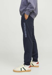 Pantalones de chándal azul marino con un logo vertical "JACK&JONES" en gris claro. Hechos de tela suave, con una cintura elástica y puños.