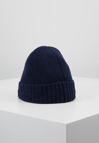Navy knitted beanie with a ribbed texture, featuring a folded cuff. Made of warm material, it has a rounded top and subtle branding detail.