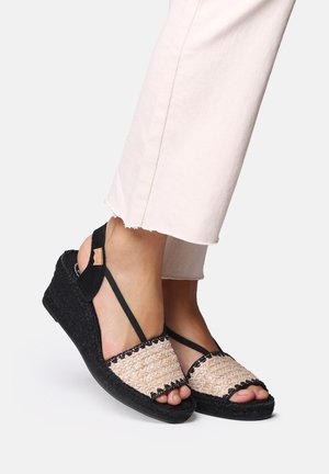 Black wedge sandals with woven beige strap, open-toe design, and adjustable black ankle straps. Textured sole and decorative black trim.
