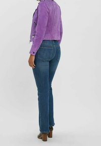 Paarse suède jas, getailleerd ontwerp, kort model; gecombineerd met blauwe denim jeans, rechte pijpen, medium wasbeurt, zichtbare achterzakken.