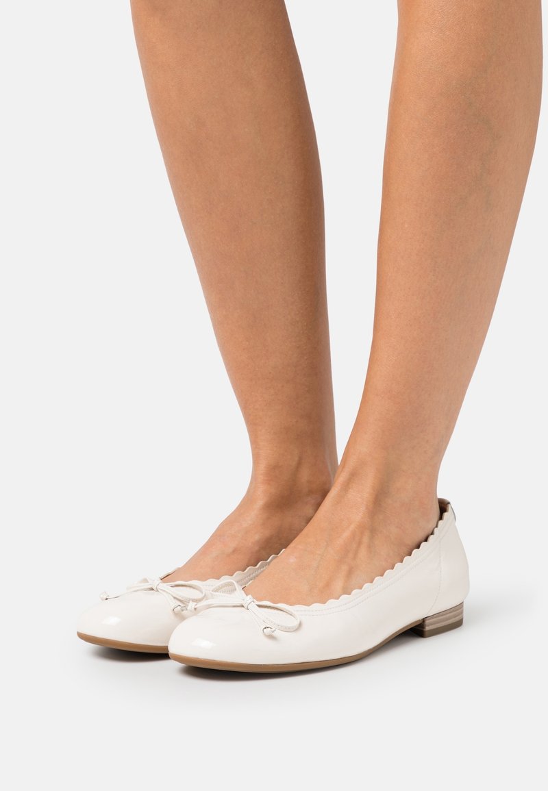 Ballerines en cuir verni blanc avec des bords festonnés, un nœud attaché au niveau des orteils et un petit talon empilé.