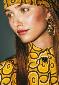 Blouse jaune à motifs circulaires, détails de boutons noirs, et foulard assorti jaune. Boucles d'oreilles dorées ornées avec des accents foncés.