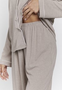 Conjunto de pijama de canalé beige con ribetes blancos, que incluye una blusa con botones y pantalones con cintura elástica. La suavidad del tejido es evidente.