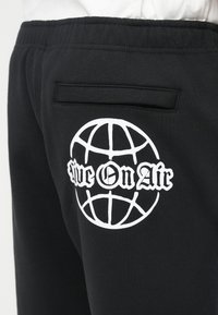 Μαύρο παντελόνι φόρμας με λευκό γραφικό με παγκόσμια υδρόγειο και κείμενο "Ζήσε στον Αέρα". Διαθέτει πίσω τσέπη και απαλό, υφασμένο ύφασμα.