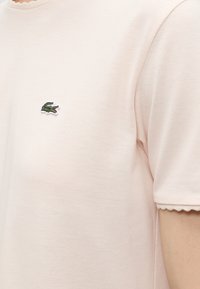 Chemise en tissu texturé rose clair à manches courtes avec un petit logo crocodile vert brodé sur la poitrine.