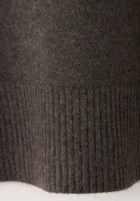 Gros plan d'un tissu en laine tricotée brun foncé montrant des fibres fines et un ourlet côtelé en bas.