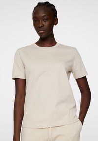 Kortärmad beiget t-shirt, rund halsringning, mjukt bomullstyg, minimalistisk design, med en liten logotyp tryckt på bröstet.