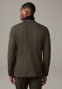 Olivgrüner Anzugjacke mit strukturierter Oberfläche, ausgestattet mit einem schwarzen Kragen, Schlitz hinten und Knöpfen an den Ärmeln, von hinten betrachtet.