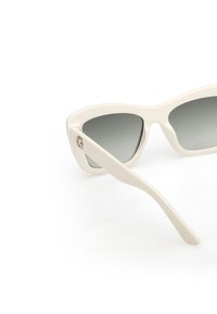 White cat-eye sunglasses with grey gradient lenses, smooth plastic frame, and slender arms featuring a small logo accent on one side.