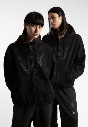 Black zip-up hoodies feature a front pocket and an abstract grey graphic on the chest. The fabric appears soft with a relaxed fit.