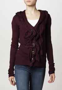 Bordowy sweter kardigan z przodu z falbanką, głębokim dekoltem w serek i zapięciem na guziki. Posiada kaptur i długie rękawy. Gładka faktura.