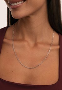 El collar de cadena de plata presenta eslabones alargados, que se lleva cerca del cuello, destacando una textura suave y un diseño minimalista.