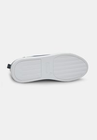 Talpa unei adidaș, cu o bază din cauciuc alb, având modele texturate pentru aderență și o secțiune superioară navy aproape de călcâi, prevăzută cu un tab de tragere în formă de buclă.