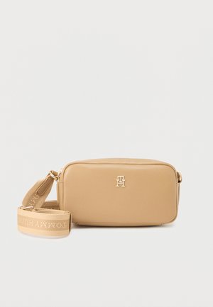Beige rektangulær crossbody-taske med guldlogo foran og justerbar stofrem lagt ved siden af på hvid baggrund.
