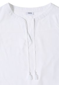 Blouse blanche avec encolure ronde et deux liens à pampilles suspendus, étiquetée avec l'étiquette de marque "CECIL" à l'intérieur du col.