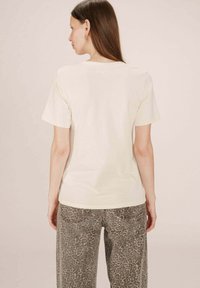 T-shirt beige clair à manches courtes et col rond, associé à un pantalon gris à imprimé léopard au style décontracté et avec poches.