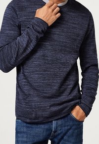 Maglietta a maniche lunghe blu navy con una finitura testurizzata e melangiata, con colletto rotondo, abbinata a denim. Presenta una vestibilità slim e polsini a coste.
