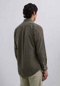 Olive green corduroy shirt with long sleeves, button-down collar, back pleat detail, and cuffs fastened by buttons.