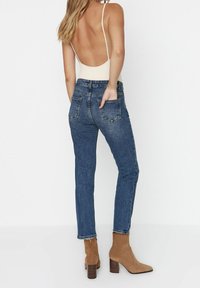 Vaqueros de denim en azul oscuro con un diseño ajustado, que cuentan con bolsillos traseros y dobladillos deshilachados, combinados con botas de ante marrón claro hasta el tobillo.