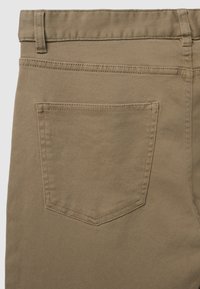 Pantalon en coton khaki avec une poche arrière unique dotée d'une couture renforcée. La texture est lisse avec un léger extensibilité.