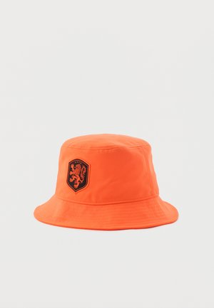 Svijetlo narančasti šešir s crnim zakrpom s likom lava i natpisom "KNVB" sprijeda na jednobojnoj pozadini.