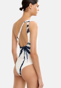 Jednoczęściowy strój kąpielowy w kolorze kremowym z granatowym nadrukiem palmowych liści. Posiada głęboki tył i szeroki ramiączko z jednej strony. Gładki, elastyczny materiał.