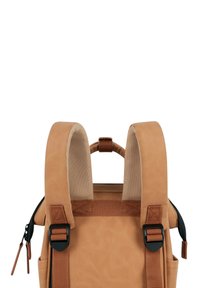 Tan backpack with padded shoulder straps and a top handle. Features textured, durable material and adjustable black hardware accents.