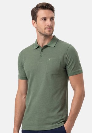 Mann mit kurzen braunen Haaren, der ein grünes Polohemd mit kurzen Ärmeln und einer Brusttasche trägt und leicht nach rechts blickt.