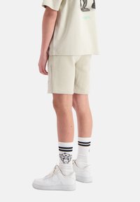 Lichtgrijze katoenen t-shirt, lose fit, met grafisch ontwerp; bijpassende lichtgrijze shorts; witte sneakers; gestreepte sokken met grafisch detail.