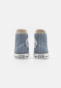 Blå canvas högskurna sneakers med vit gummisula, svarta accenter och cirkulär logotyp på varje sida. Sömmar längs kanterna.