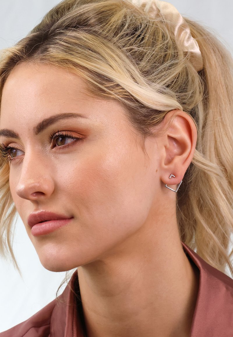 Silberne geometrische Ohrringe mit einem dreieckigen und L-förmigen Design. Glatte Metalloberfläche, minimalistische Stil, getragen von einem Model.