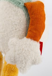 Plush toy with fluffy white fur, orange corduroy accents, and a mint green patch. Notable soft texture and star-shaped detail on the hand.