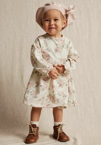 Blommig klänning i off-white tyg med rosa rosor, samlade ärmar och en volangkant. Kombinerad med bruna snörboots och en rosa basker.