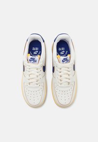 Zapatillas de cuero blanco con acentos azules, caja de dedos perforada y suelas color crema. Presentan una plantilla azul etiquetada y cordones blancos.