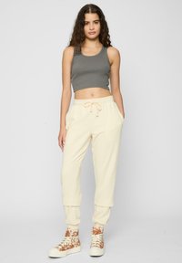 Lichtbeige sweatpants met een drawstring, met cuffed enkels, gecombineerd met een strakke grijze crop top en patroon hoge sneakers.