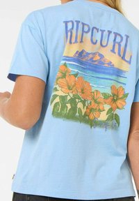 Lysblå bomuld t-shirt med et farverigt grafisk design af bjerge, hav og orange blomster. "RIPCURL" tekst i fede bogstaver.