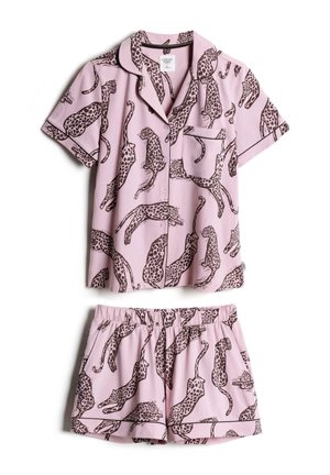 Jeune femme aux longs cheveux noirs portant un t-shirt rose à manches courtes avec un motif léopard noir, regardant sur le côté.