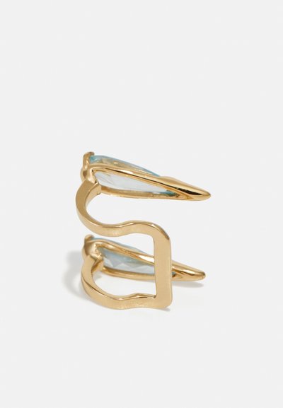 Gold-tone ring featuring a wavy, open design with two light blue, faceted stones set into the band, enhancing its dimensional appearance.