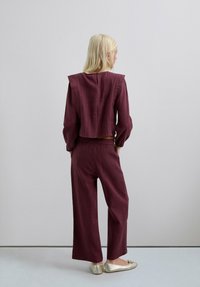 Conjunto texturizado burdeos con un top corto que cuenta con un cierre trasero y pantalones sueltos de pierna ancha. Zapatos planos metálicos completan el conjunto.