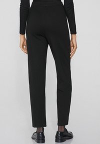 Pantalons noirs, ajustés avec une coupe droite. Fabriqués dans un tissu doux, avec une texture lisse et sans embellissements ni motifs visibles.