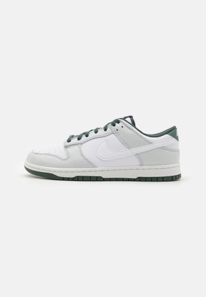 Witte en lichtgrijze Nike lage sneaker met donkergroene veters, zool, binnenvoering en zijkant Swoosh-logo, zijaanzicht.